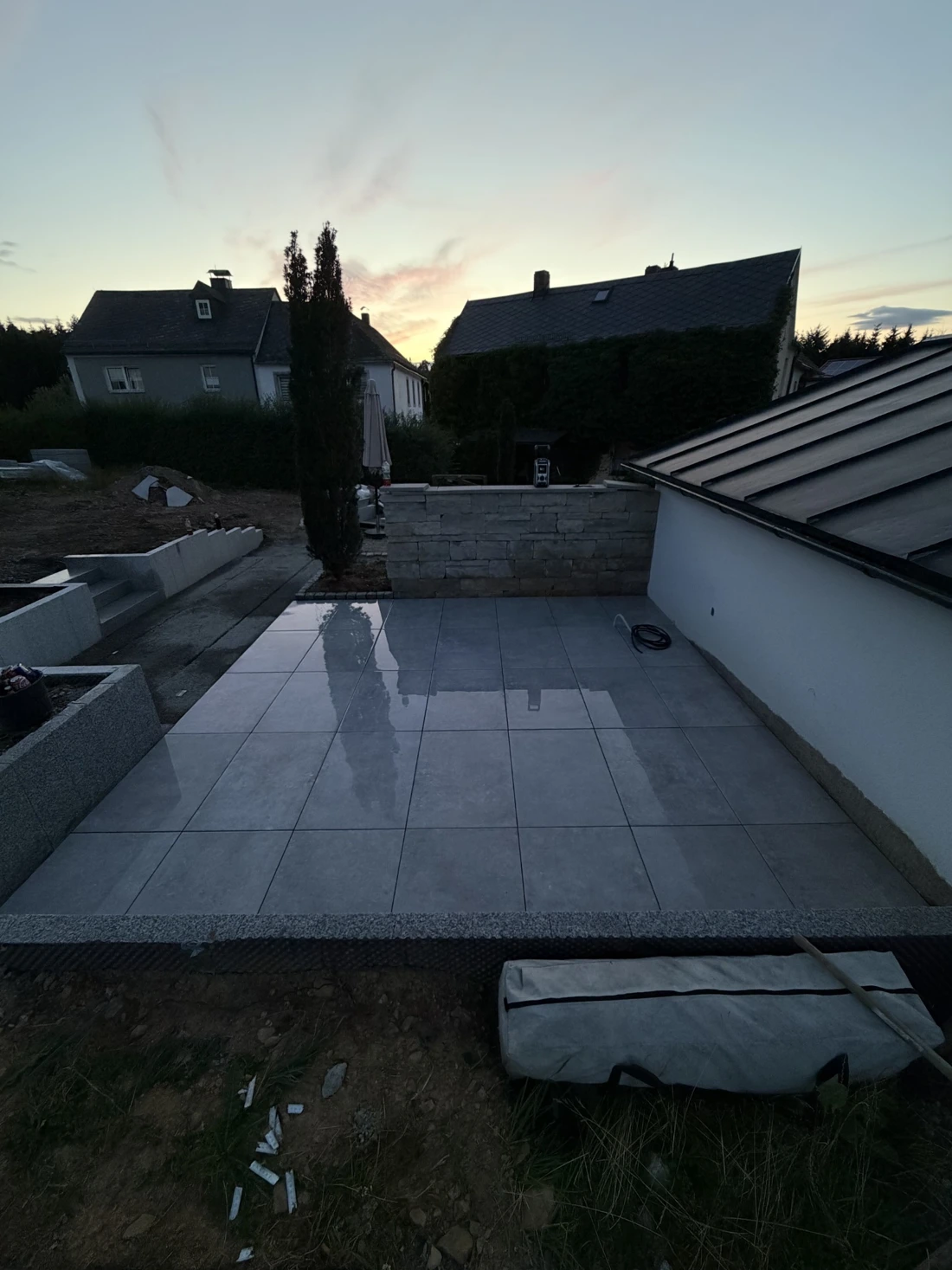 Foto einer fertig verlegten Terrasse mit großen grauen Platten und einer Steinmauer im Abendlicht